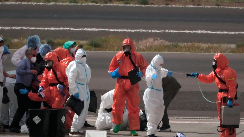 Passengers are sprayed with disinfectant by Spanish government officials before boarding a...